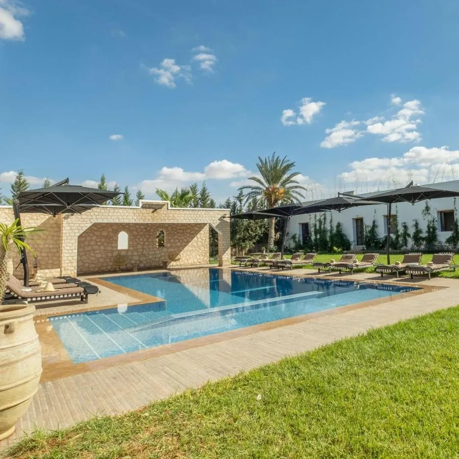 Pool at Cavanna Lodge surrounded by lawn and palm trees, in front of the lodge buildings