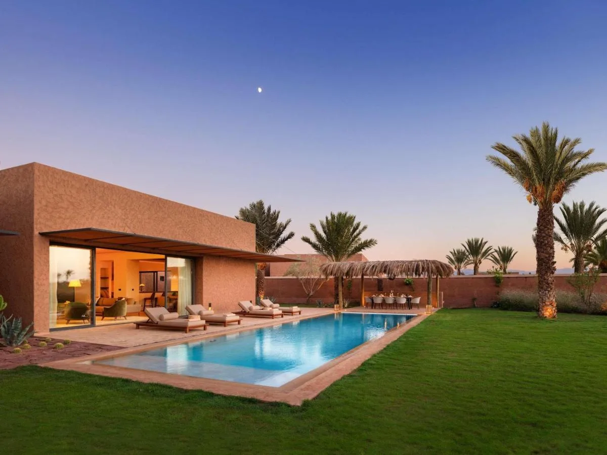 Villa des Fairmont Royal Palm Marrakech in der Abenddämmerung mit Privatpool, Rasen und Palmen