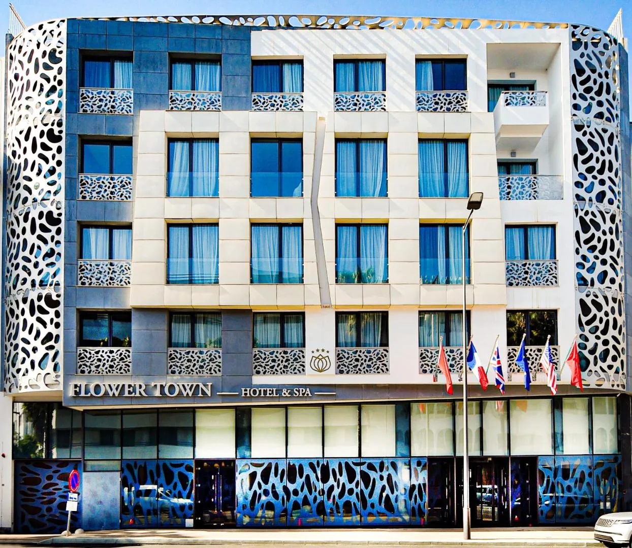 Façade of the Flower Town Hotel & Spa with perforated panels, its sign and flags