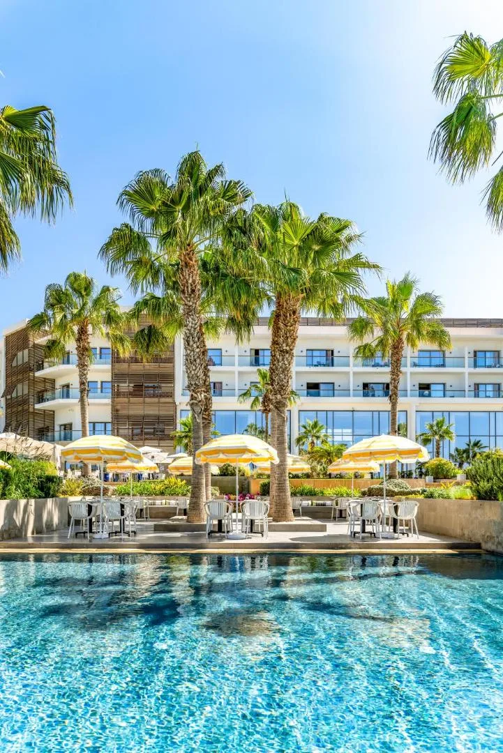 White façade of the Hyatt Place Taghazout Bay behind palm trees and yellow-and-white parasols