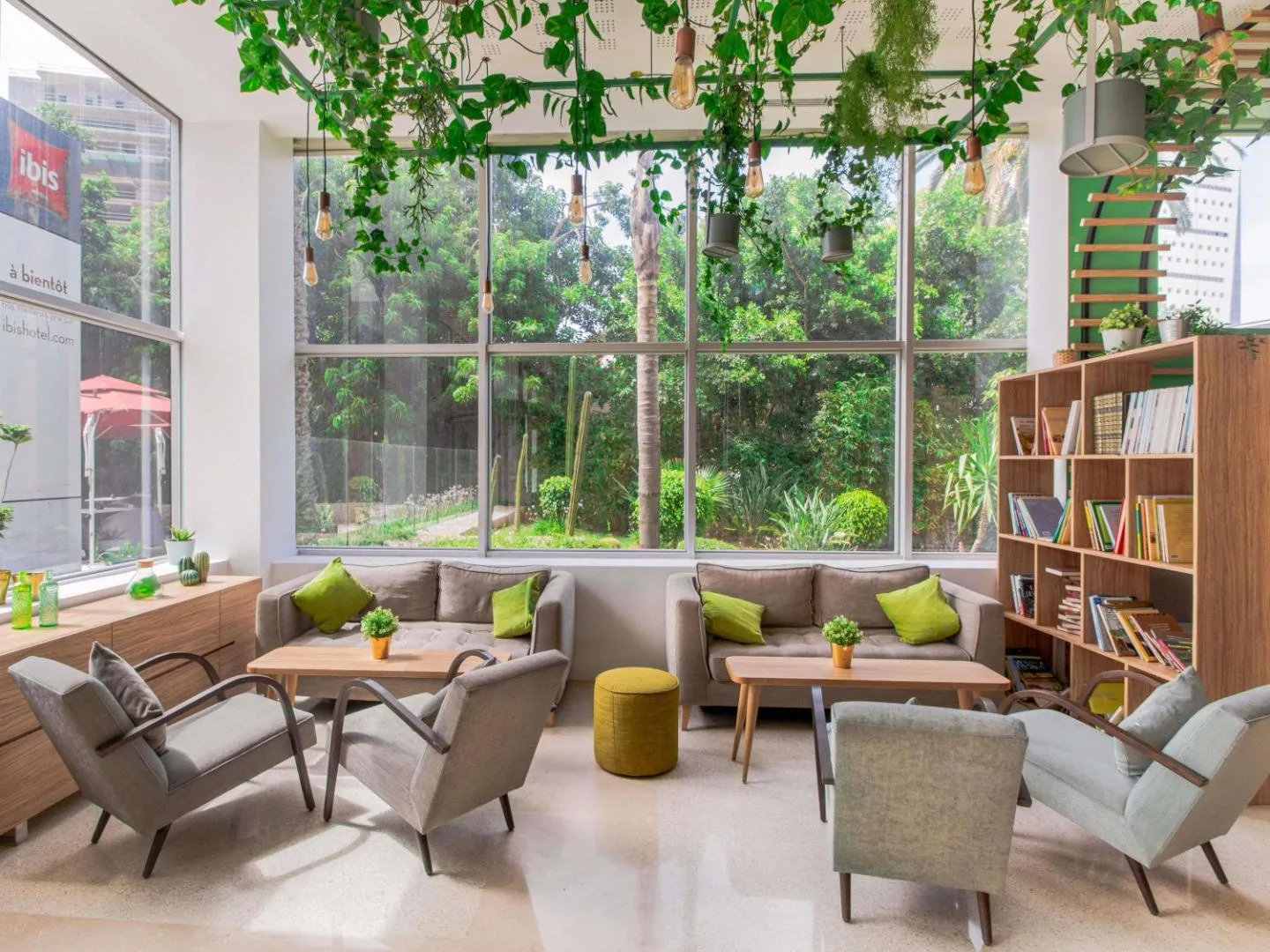 Bright lounge at the ibis Casablanca City Center, with a bookcase, hanging plants and armchairs facing the garden