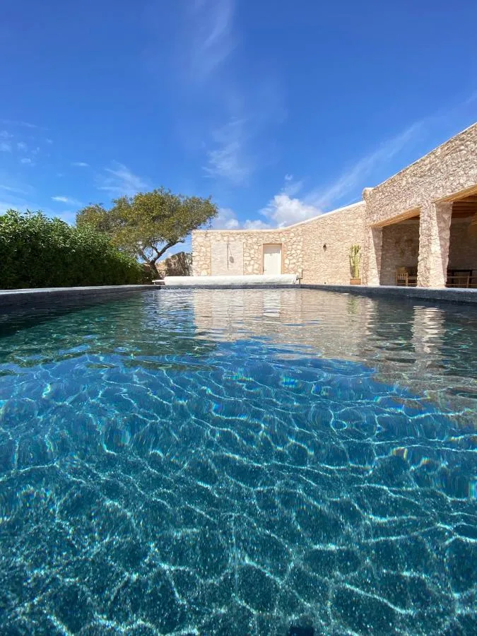 Pool at Kaouki Lodge in front of stone buildings, under a blue sky