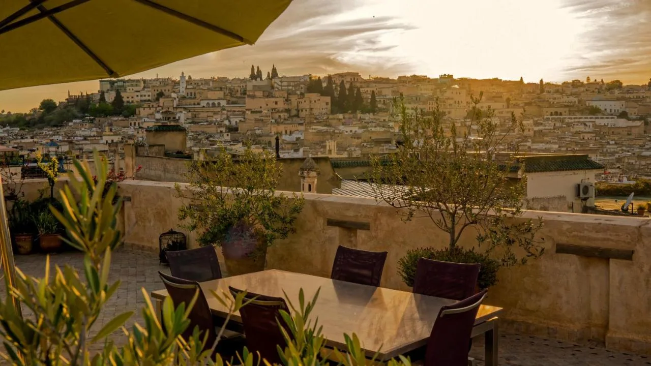 Terrasse des Karawan Riad unter einem Schirm mit Blick auf die Medina von Fès bei Sonnenuntergang