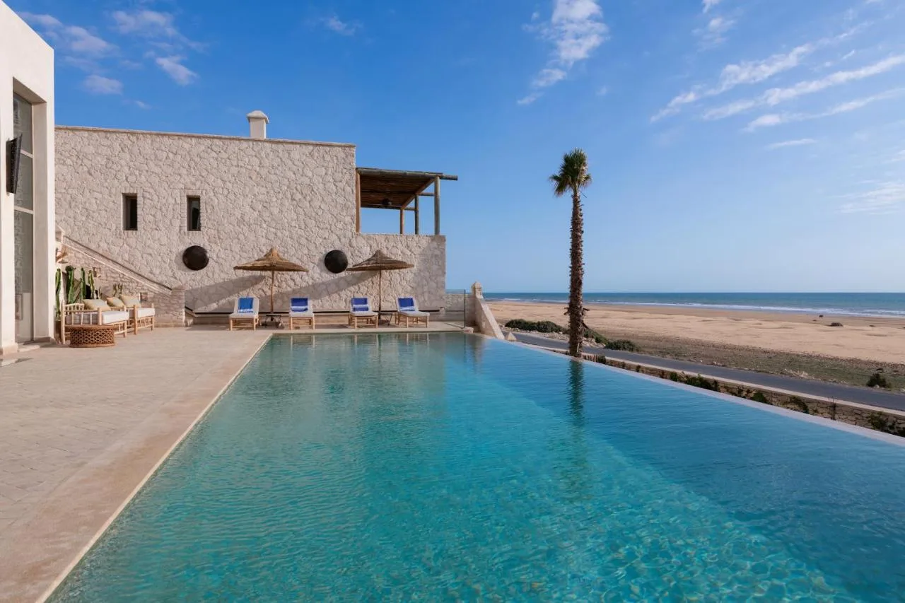Pool at Kasbah d'Eau facing the ocean, with palm trees and white buildings