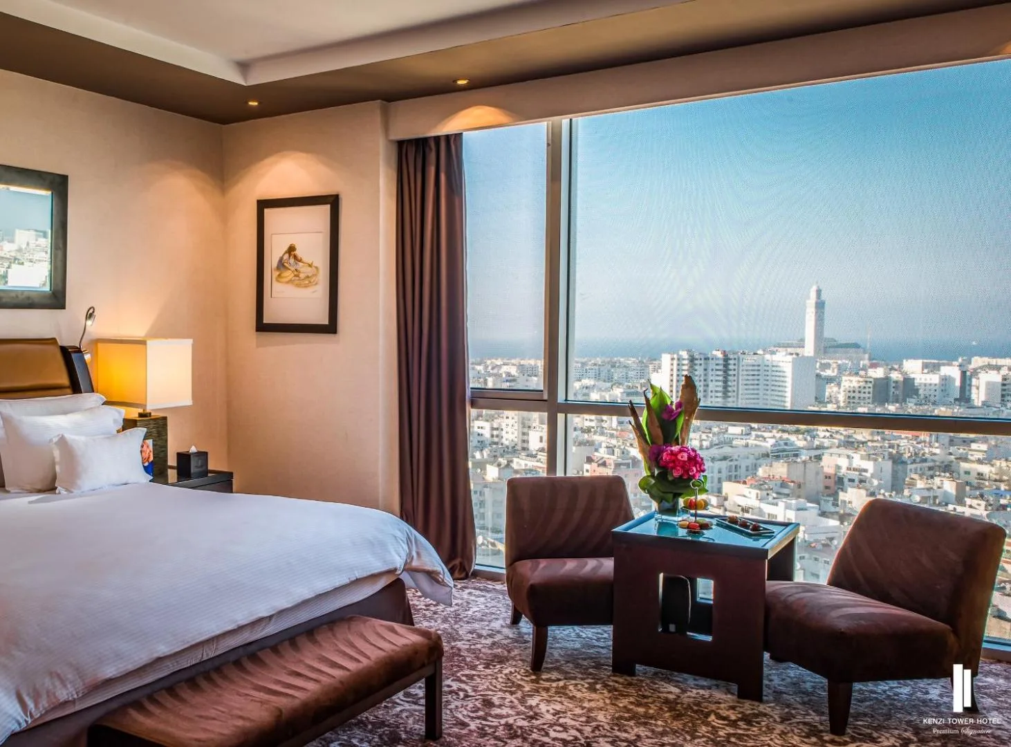 Room at the Kenzi Tower Hotel with armchairs by a picture window, overlooking the city and the Hassan II Mosque minaret