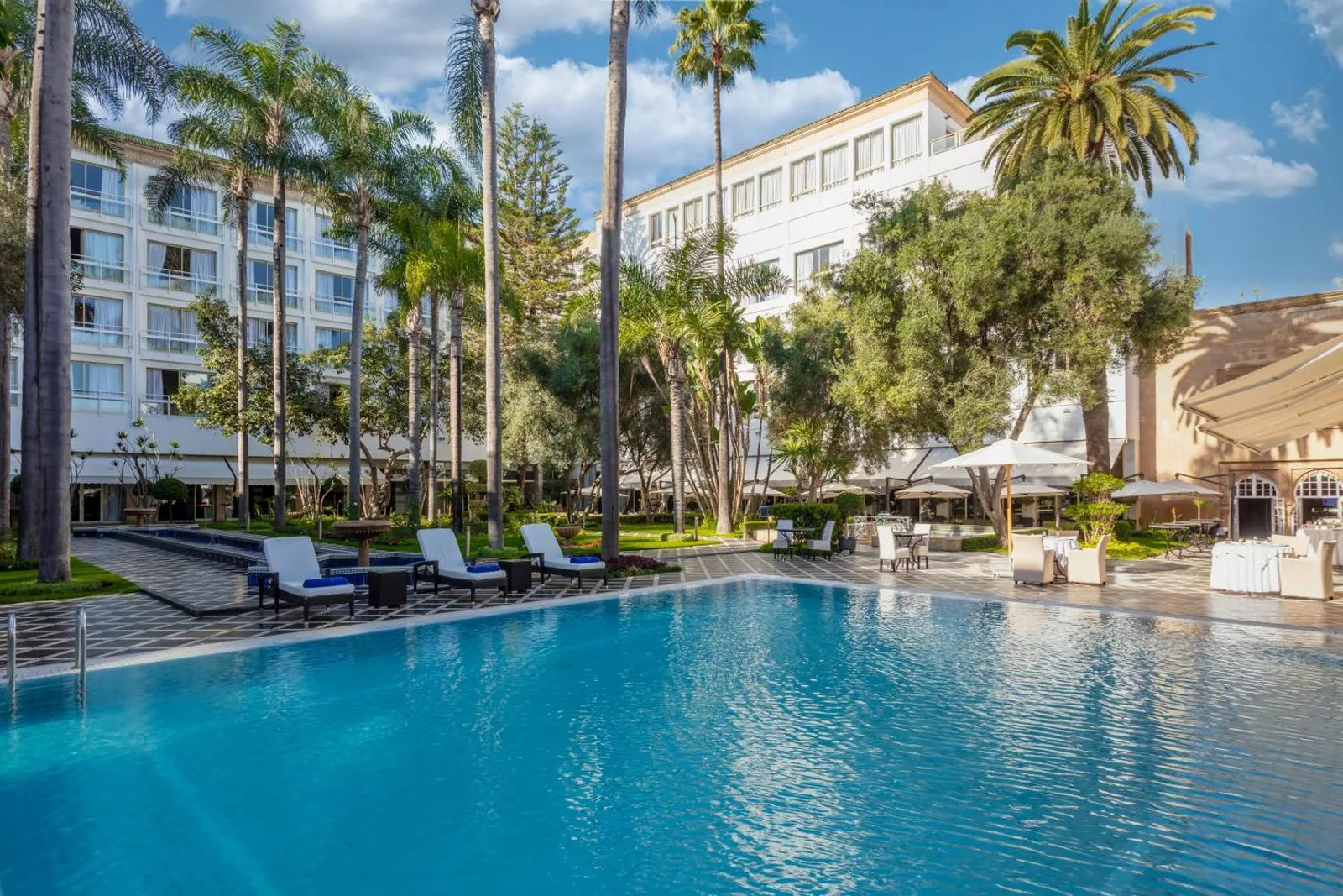 Pool and garden of La Tour Hassan Palace with the hotel building among palm trees