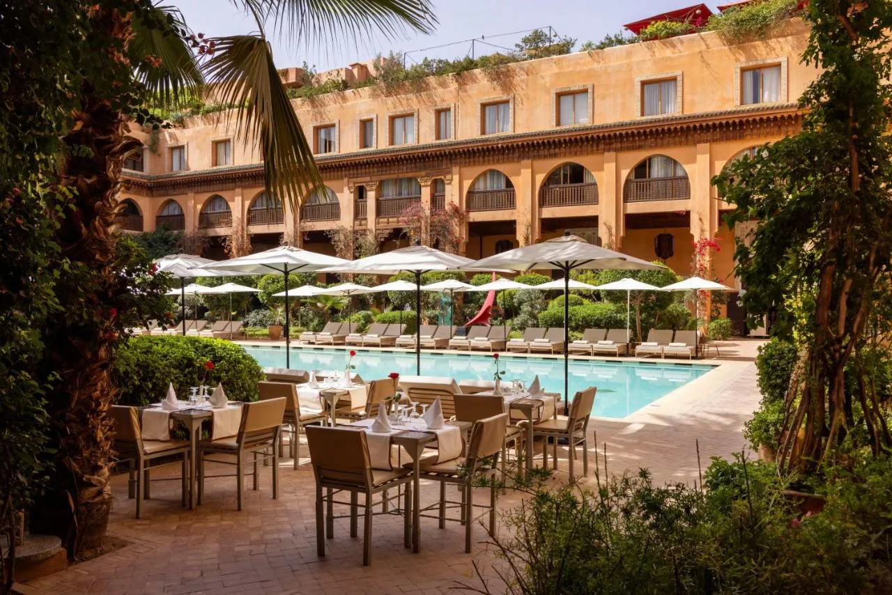 Pool der Jardins de la Koutoubia mit Sonnenschirmen und Tischen vor Fassaden mit Arkaden