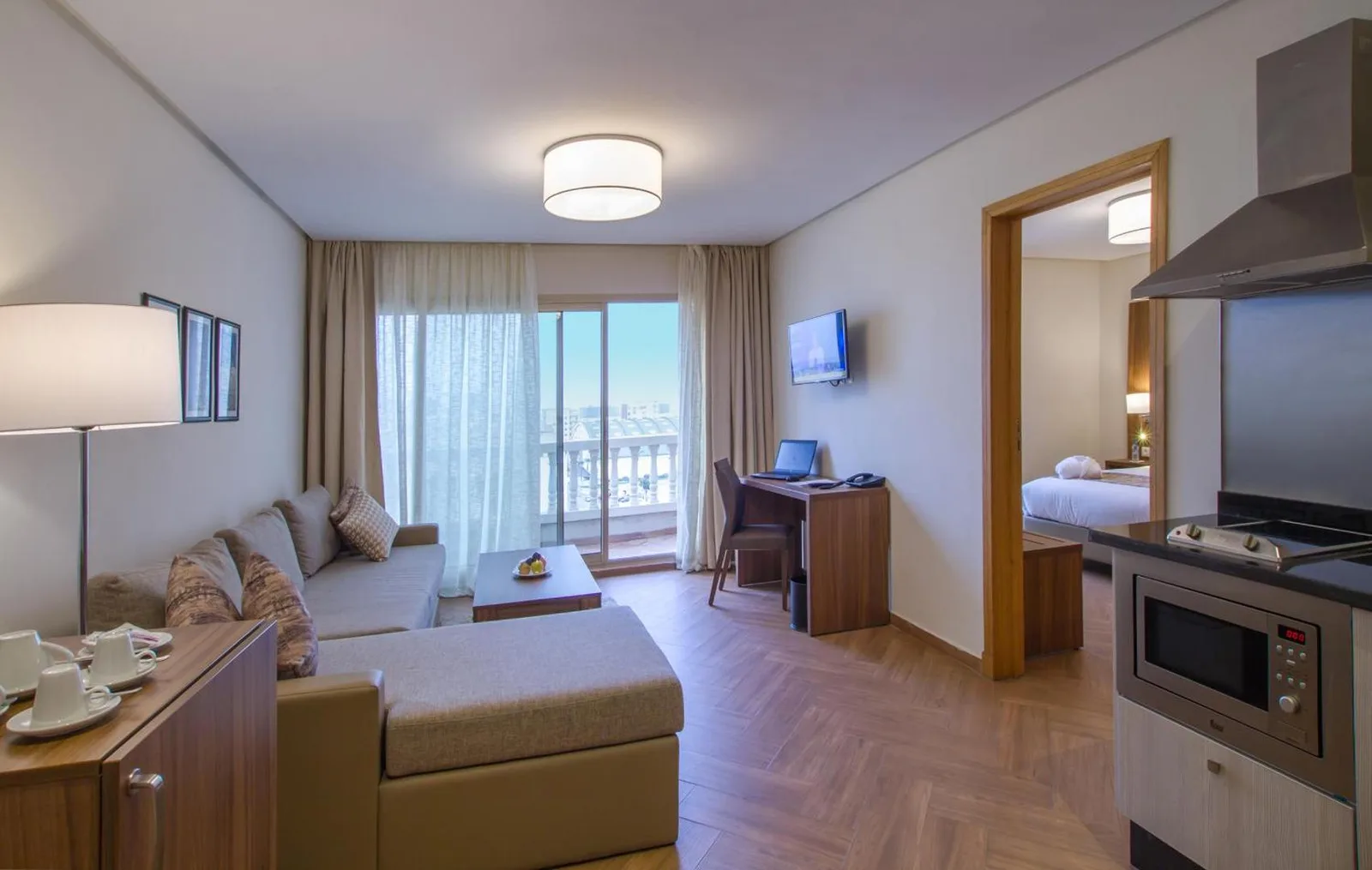 Living room of a Melliber Appart Hôtel apartment with a kitchenette, corner sofa and adjoining bedroom