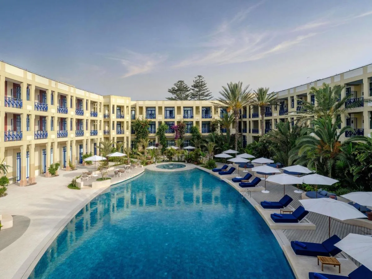 Large pool at Le Médina Essaouira MGallery surrounded by loungers, palm trees and balconied façades