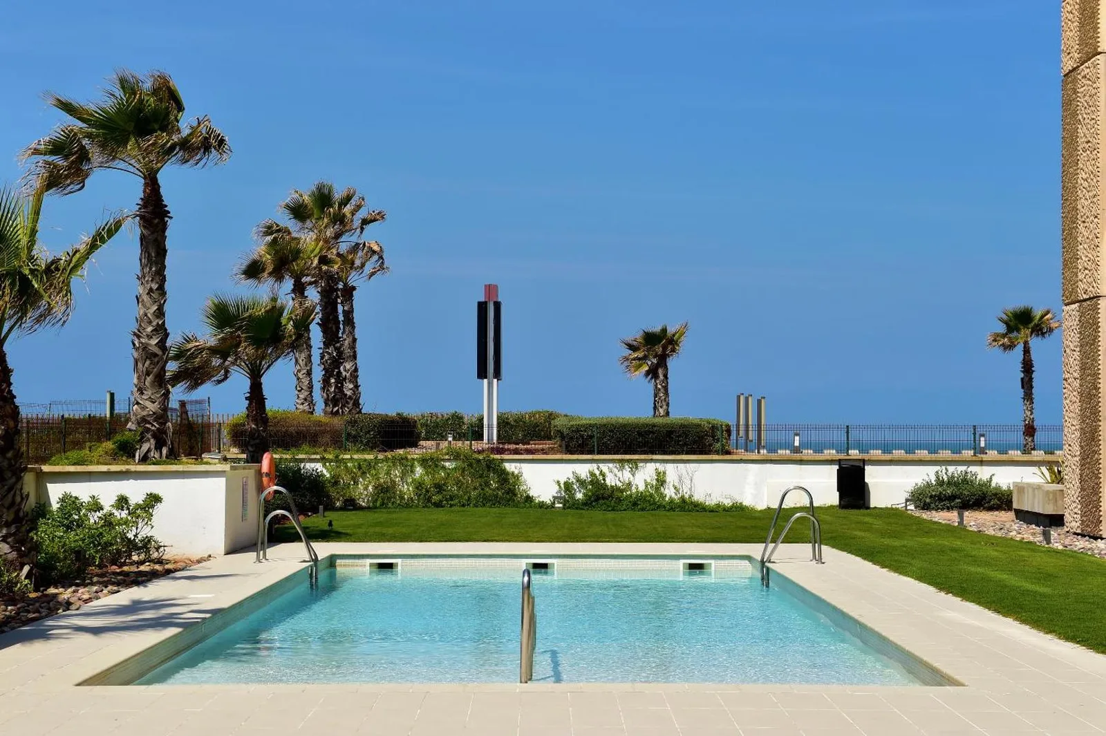 Pool surrounded by palm trees and lawn facing the ocean at the Pestana Casablanca Seaside Suites & Residences