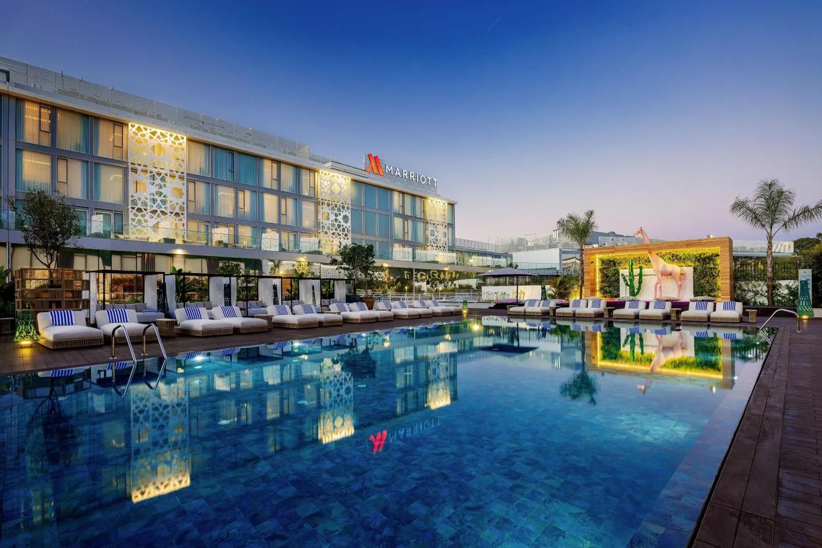 Pool of the Rabat Marriott Hotel at dusk with sun loungers and the façade decorated with perforated patterns