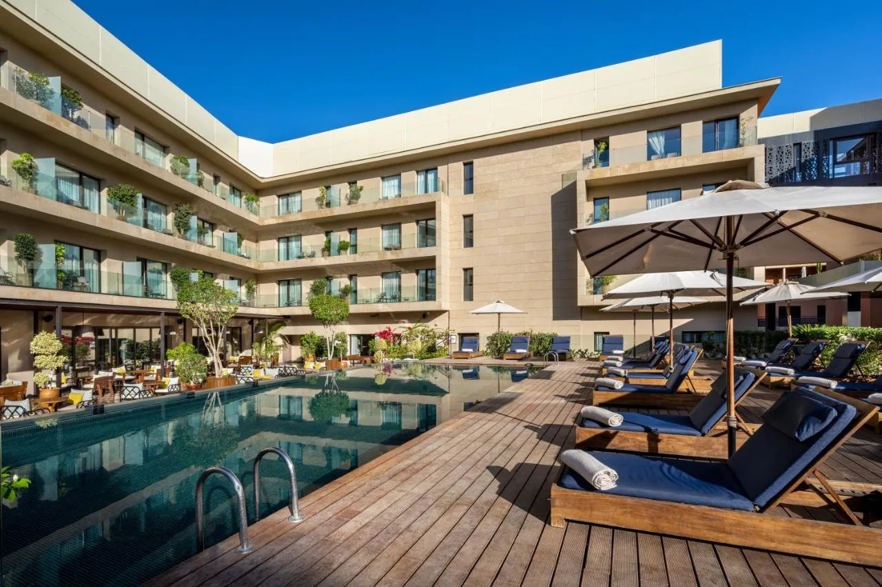 Pool des Radisson Blu Marrakech Carré Eden mit Holzdeck, Liegen und Sonnenschirmen