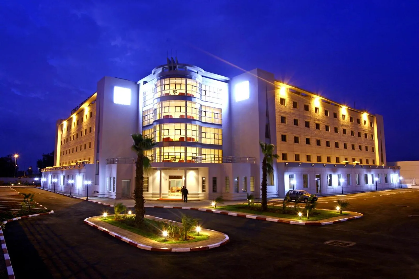 Illuminated façade of the Relax Hotel Airport Nouasseur at dusk, with its access driveway