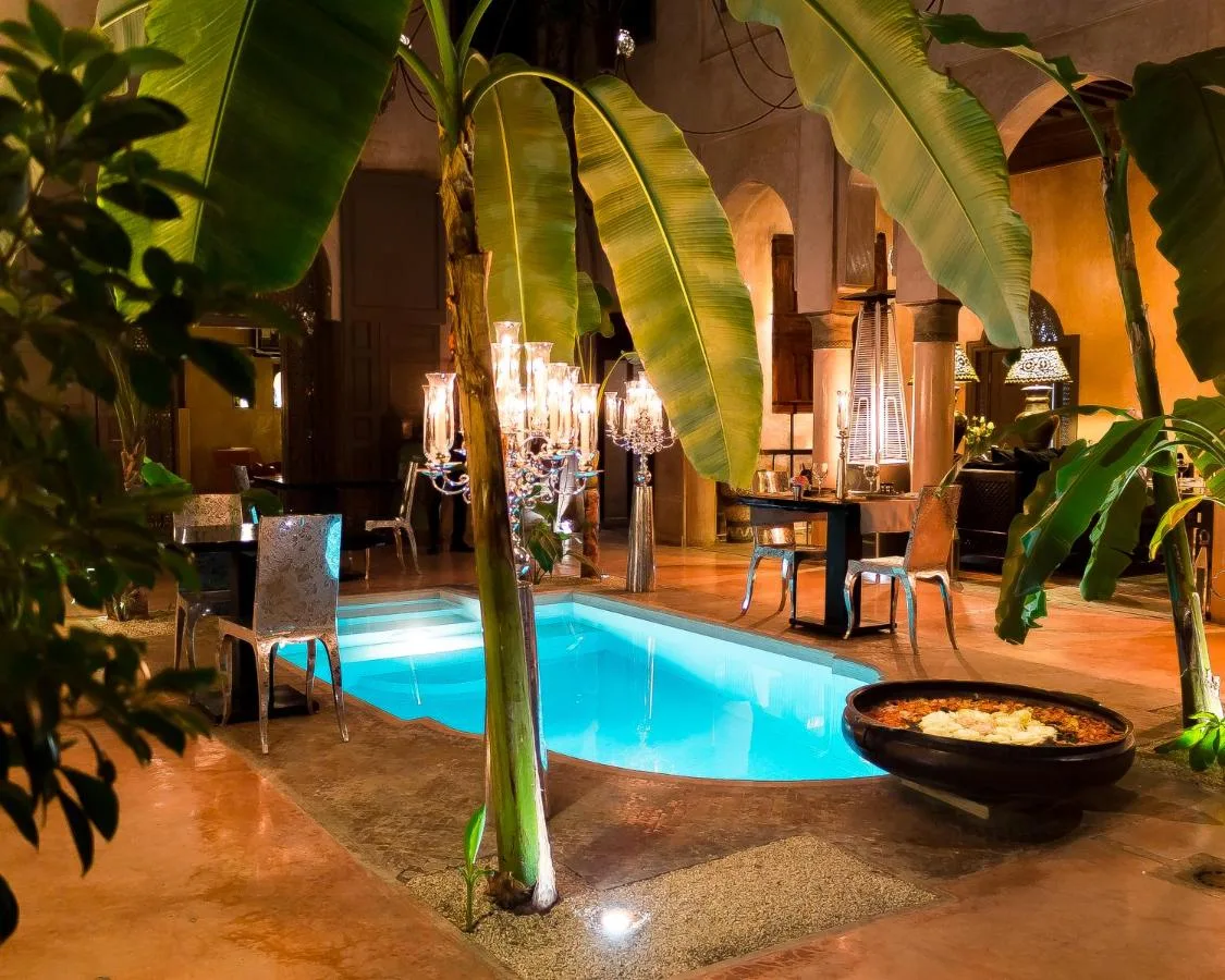 Becken im Innenhof des Riad Noir d'Ivoire bei Nacht, umgeben von Bananenstauden und Kristallleuchtern