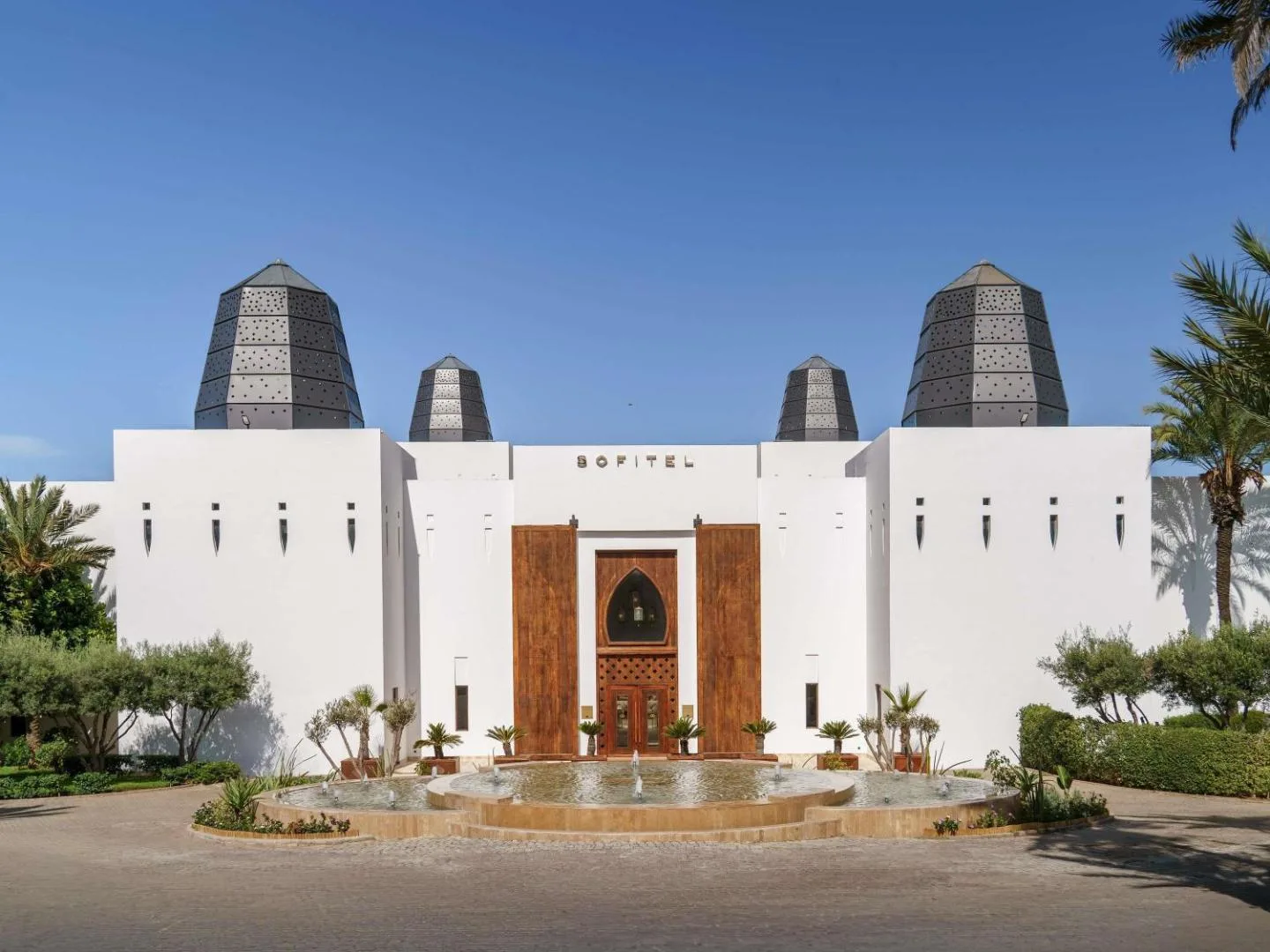 White façade of the Sofitel Agadir Royal Bay Resort with its dark lanterns, wooden doorway and fountain