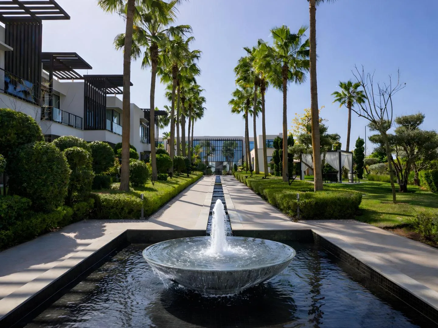 Pond with a fountain in a garden of palm trees and clipped box hedges in front of the STORY Rabat buildings