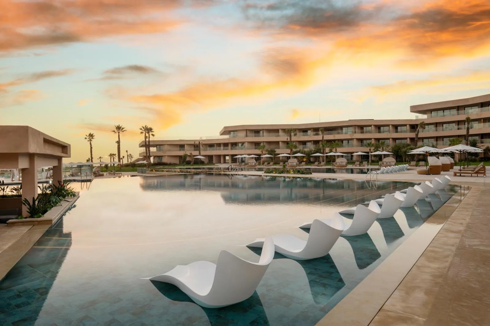 Large pool at the Taghazout Bay Marriott Resort at sunset, with white loungers and terraced buildings