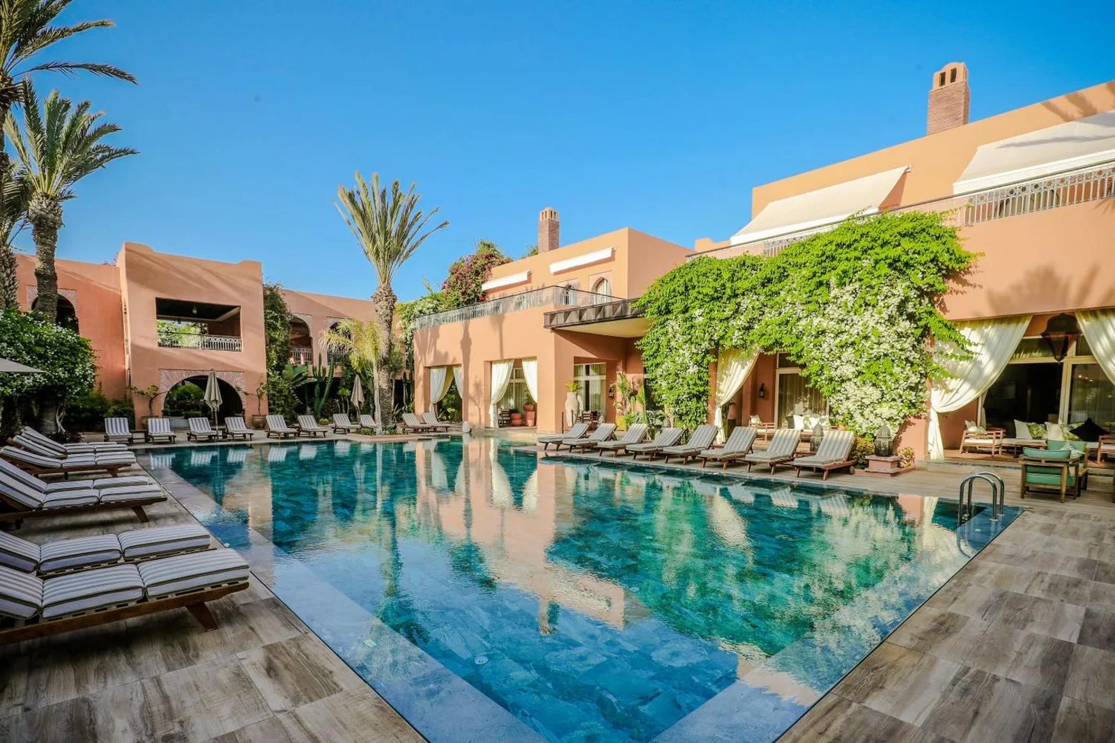 Pool and ochre buildings of the Tikida Golf Palace, surrounded by palm trees and climbing plants