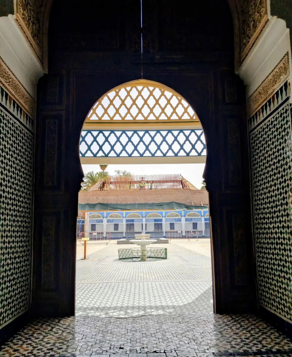 Blick durch einen von Zellige eingerahmten Bogen auf den weitläufigen Ehrenhof und seinen Brunnen im Bahia-Palast in Marrakesch.