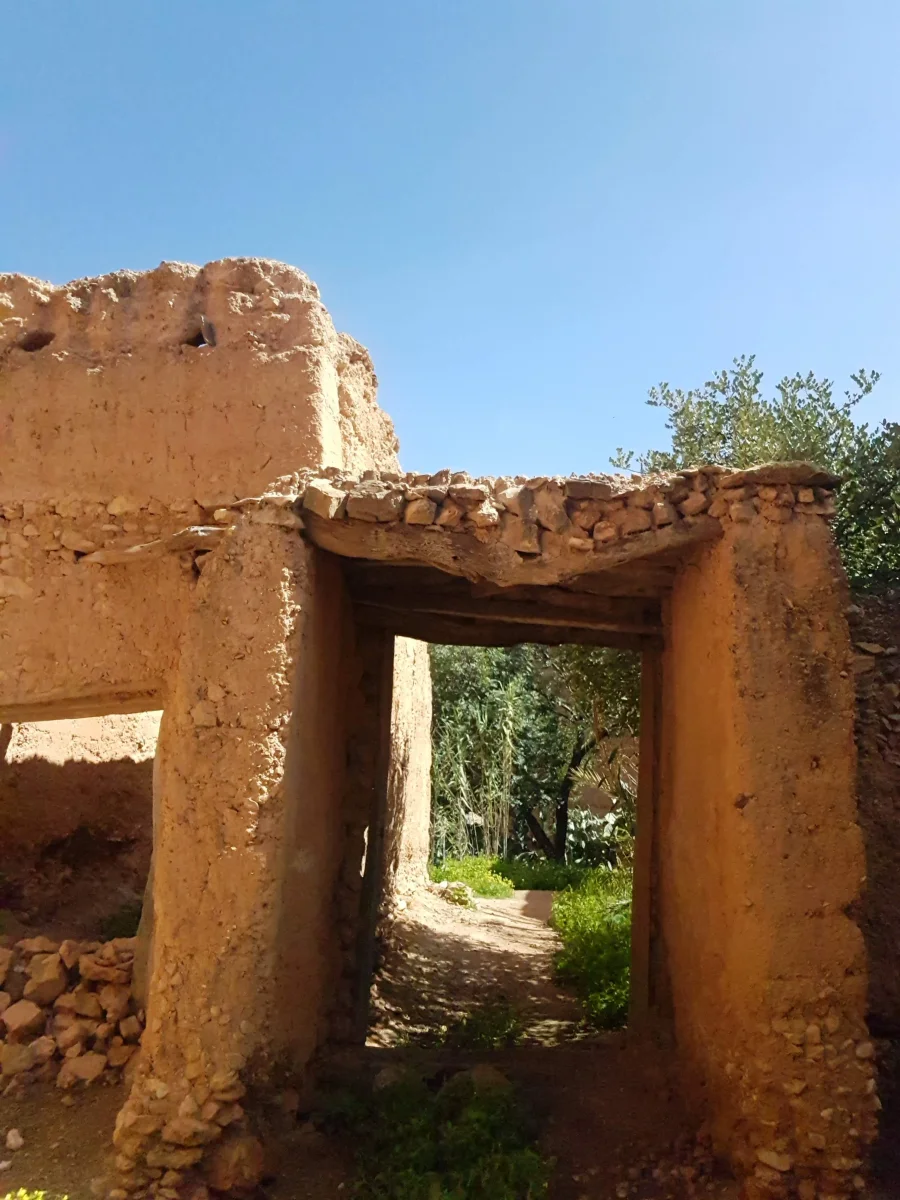 Vue d'une ancienne structure en pisé traditionnelle marocaine avec une porte d'entrée rustique et des murs en terre crue.