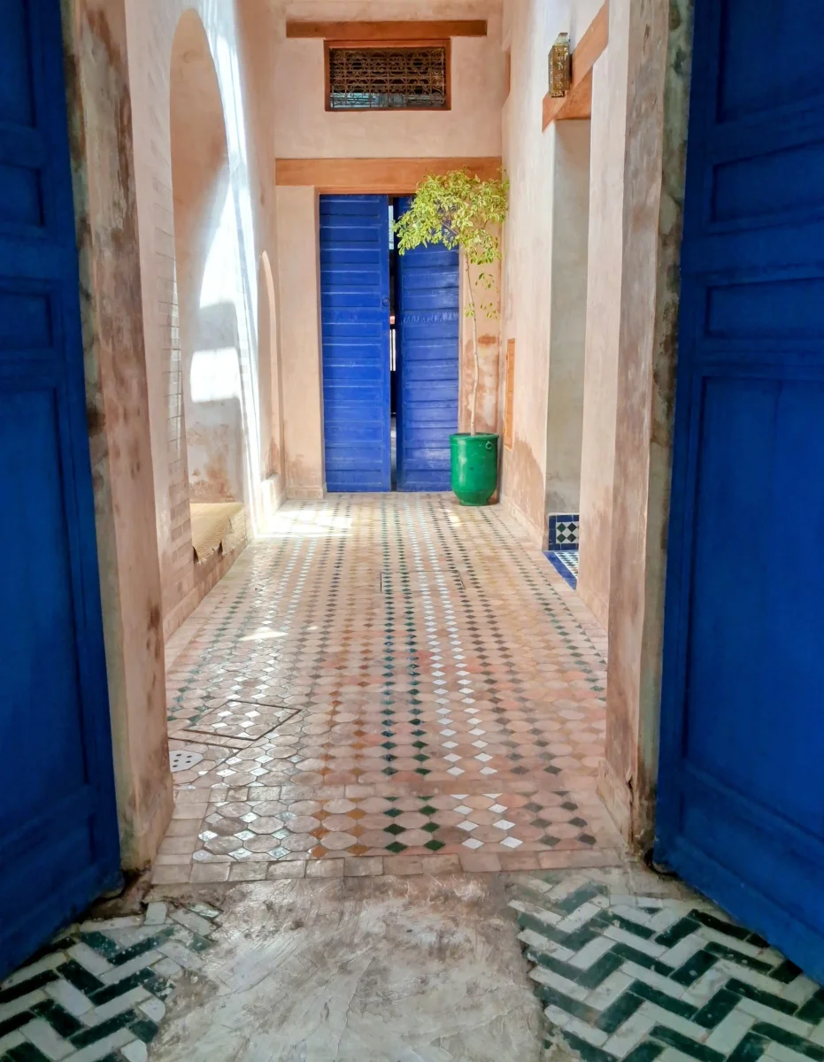 Détail d'une allée dans le Palais de la Bahia, Marrakech, avec des portes bleues distinctives et un sol en zellige marocain géométrique.