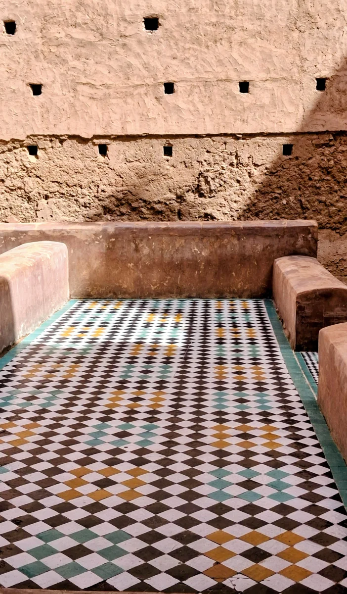Close-up of a Moroccan zellige floor with complex colourful geometric patterns surrounded by rammed-earth architectural elements at El Badi Palace in Marrakech.