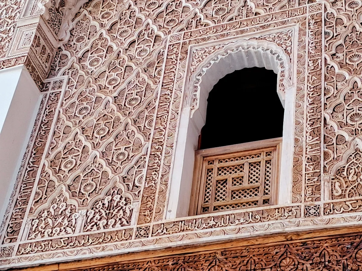 Details of carved gebs stucco and a finely worked wooden window in the architecture of the Ben Youssef Madrasa in Marrakech.