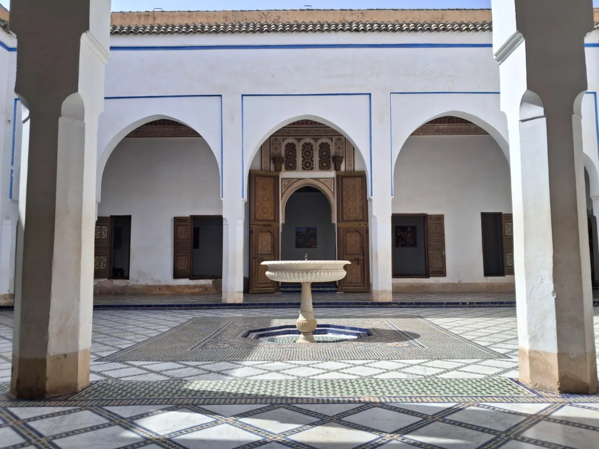 Vue d'une cour intérieure du Palais de la Bahia à Marrakech, mettant en valeur une fontaine centrale entourée d'arcades traditionnelles et de colonnes blanchies à la chaux.