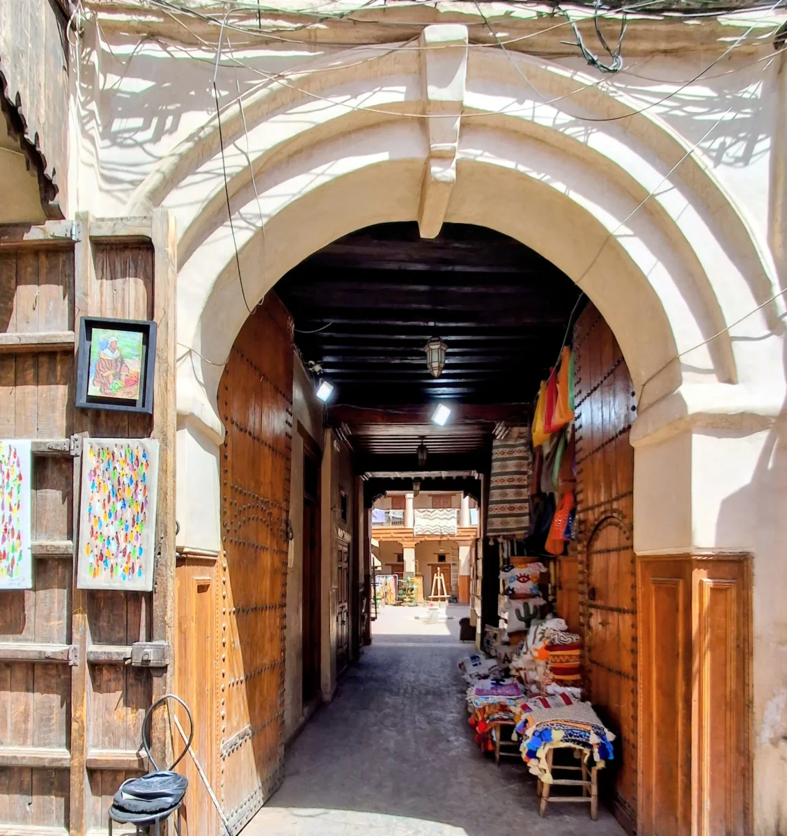 Gewölbter Eingang und Holztüren eines traditionellen historischen Funduqs im belebten Mouassine-Viertel von Marrakesch.