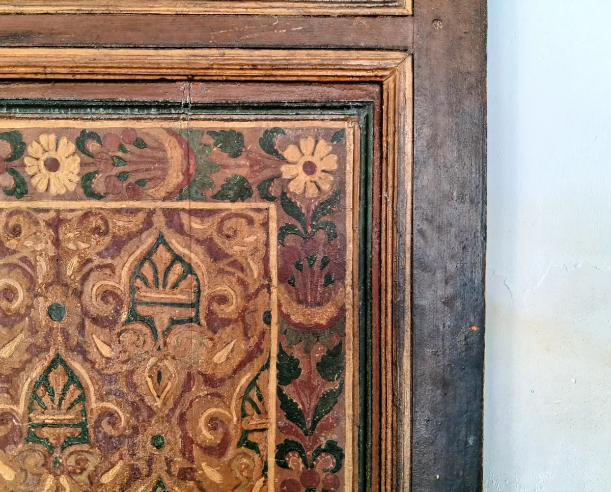 Nahaufnahme einer bemalten Holztafel im traditionellen marokkanischen Zouaq-Stil mit polychromen floralen und geometrischen Motiven.