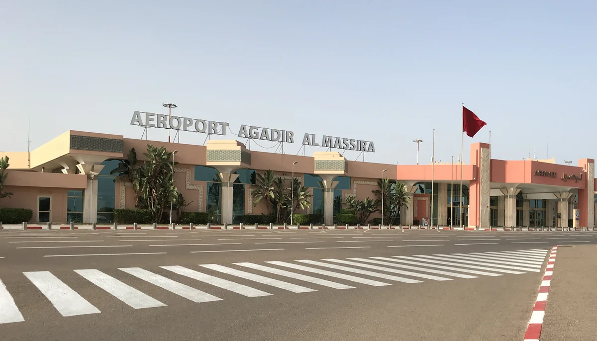 Main entrance of Agadir-Al Massira Airport, showing the airport name, pedestrian crossing and Moroccan national flag